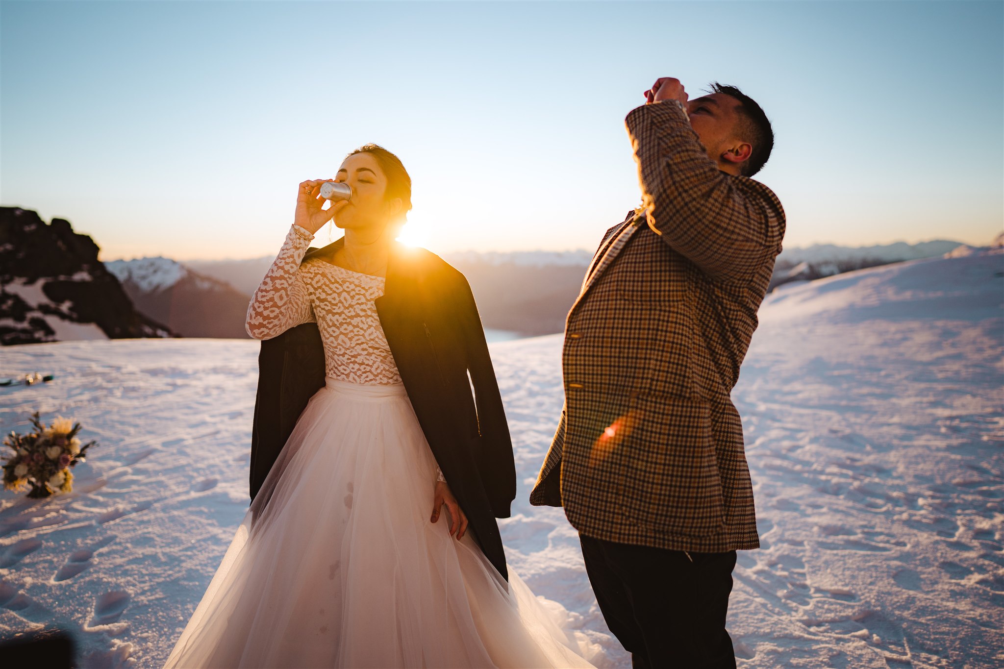 bride and groom drink shots on mountain top in the snow after wedding ceremony in Queenstown, New Zealand