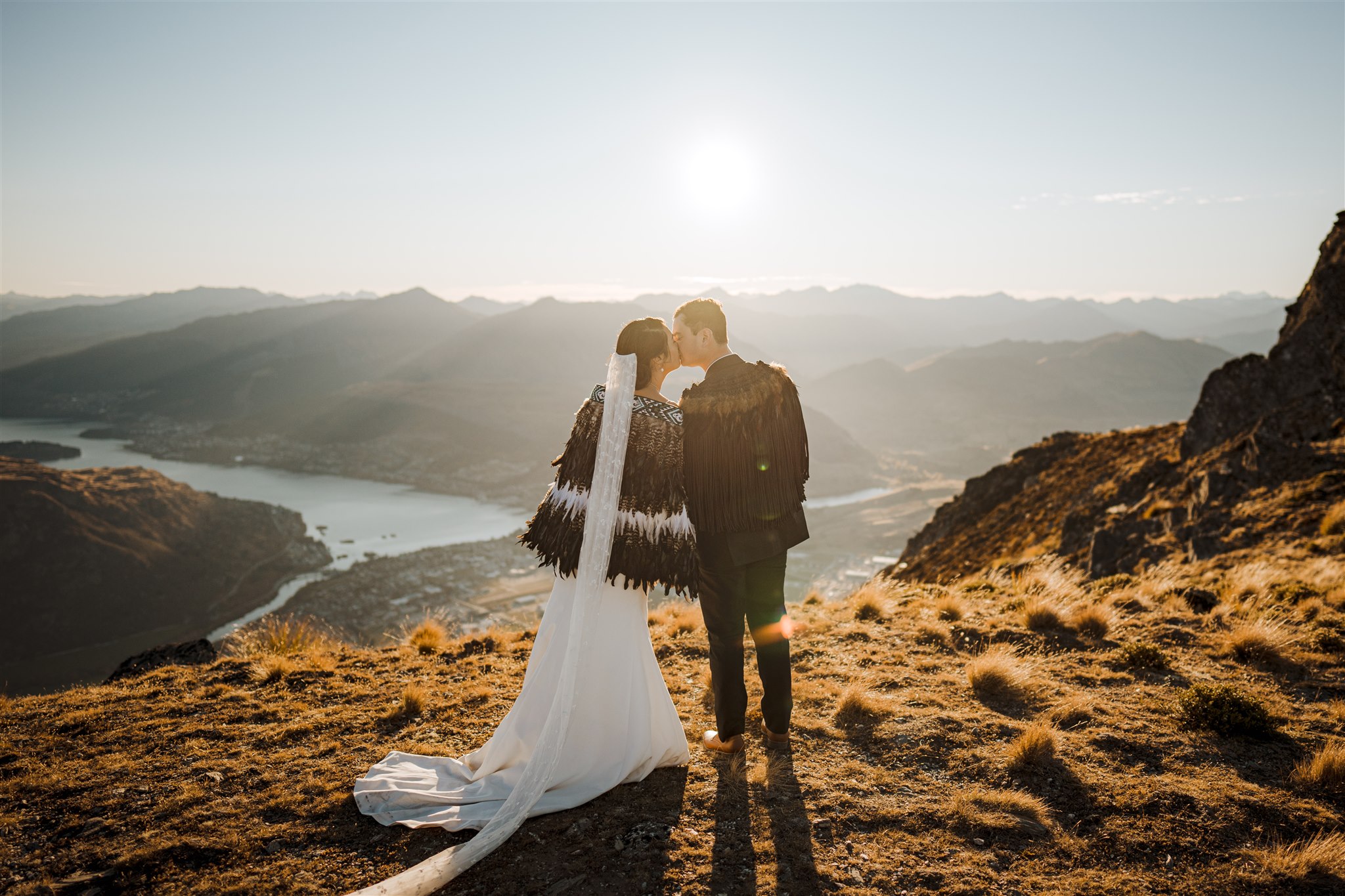 maori couple wearing korowai and kissing at sunset overlooking  Queenstown, New Zealand